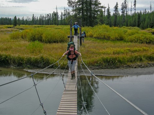 hikers crossing creek on slat bridge with cable handrails 