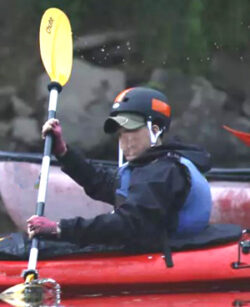 person in a kayak with a helmet on but with a hat under the helmet