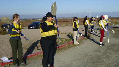people standing in a row practicing using kayak paddles