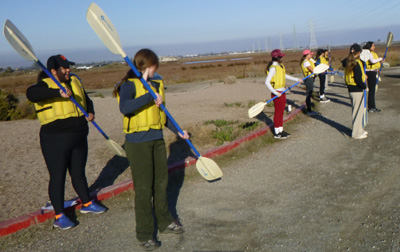 people standing in a row practicing using kayak paddles
