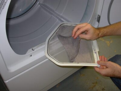 hand removes lint from a clothes dryer