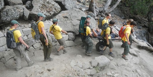 many people guiding a rescue litter down a trail