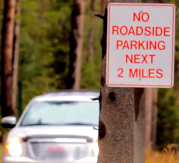 car on road and sign that says no roadside parking next 2 miles