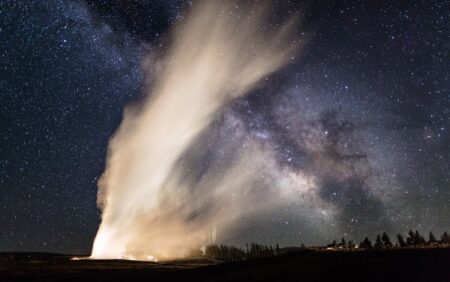old faithful eruption with milky way in sky in background
