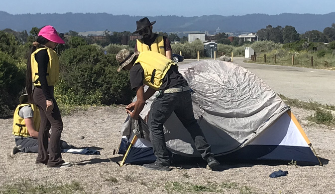 2 people watch as 2 others put rainfly on tent