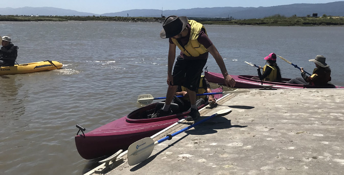 man steps into kayak as partner in kayak holds cleat built into deck