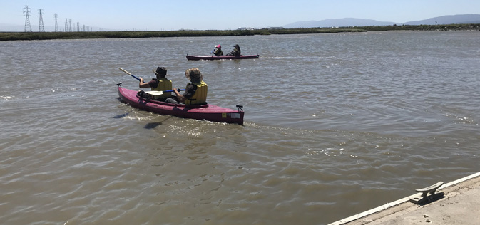 two kayaks paddle away from a dock on a large expanse of water