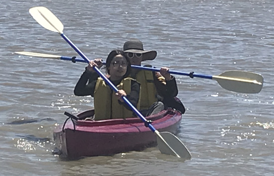 person in front of kayak paddling while person in back holds paddle up out of the water