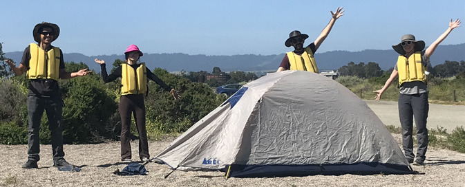 people surrounding a pitched tent with their arms in the air.