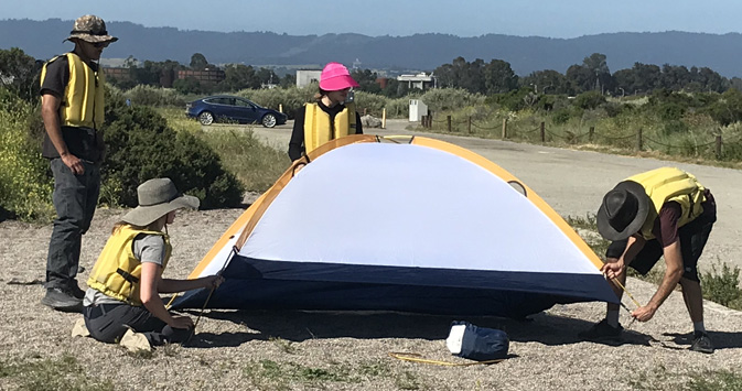 four people around a tent as one of them puts tent pole into slot