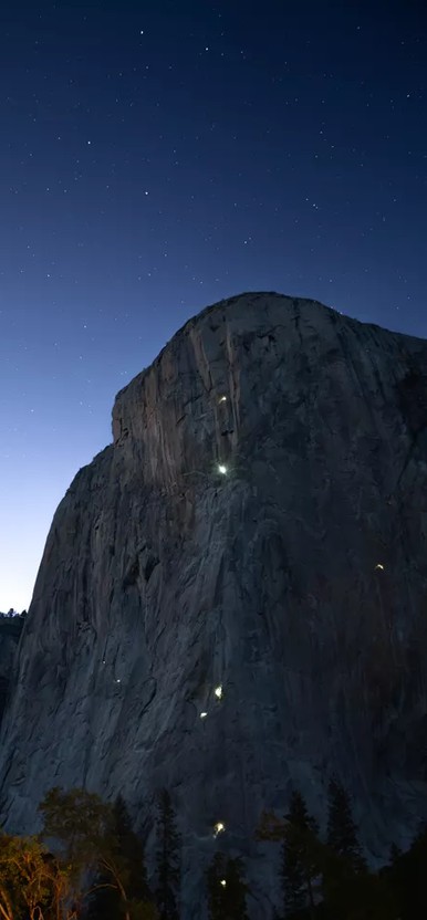 mountain face with lights from climbers head lamps just after sunset